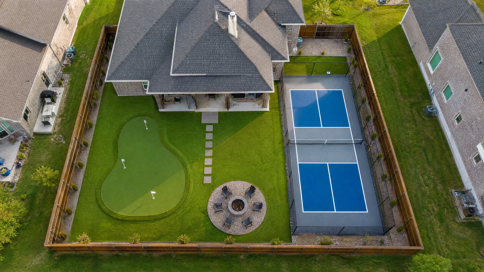 Bird's-eye view of luxury backyard with pickleball court, putting green, and fire pit