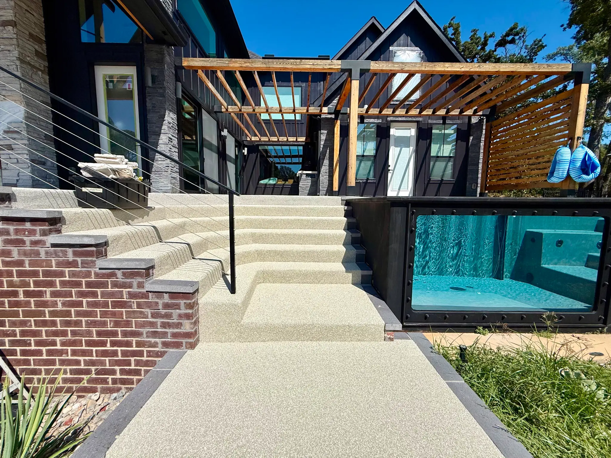 Modern home exterior with rubber-surfaced steps, pergola, and glass pool wall